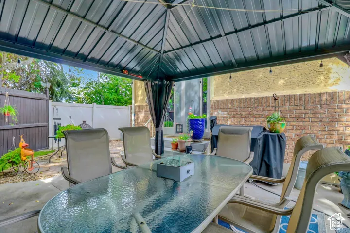 Patio area featuring a dark metal gazebo, privacy curtains, brick exterior wall, and concrete pavers