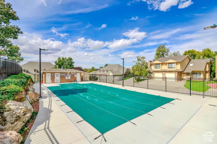 New outdoor swimming pool with a protective cover, surrounded by a concrete deck and black metal fencing