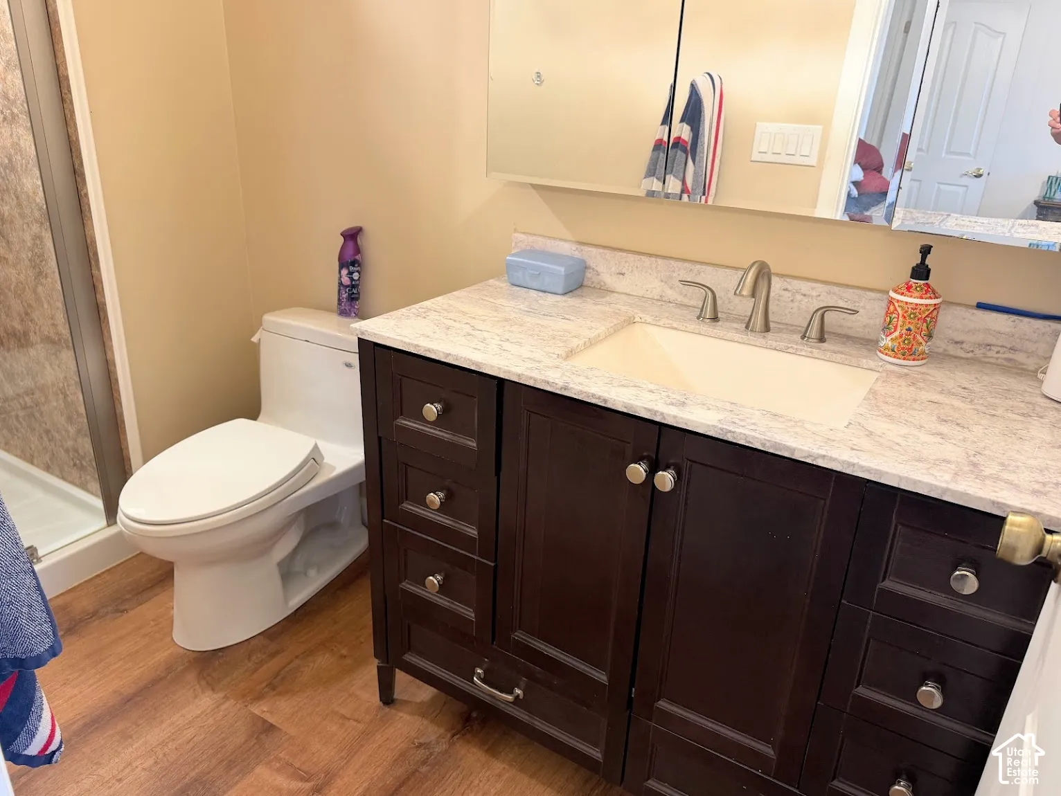 Wood-finish flooring, dark wood vanity with ample storage, integrated rectangular sink, light-colored countertop, and brushed nickel faucet