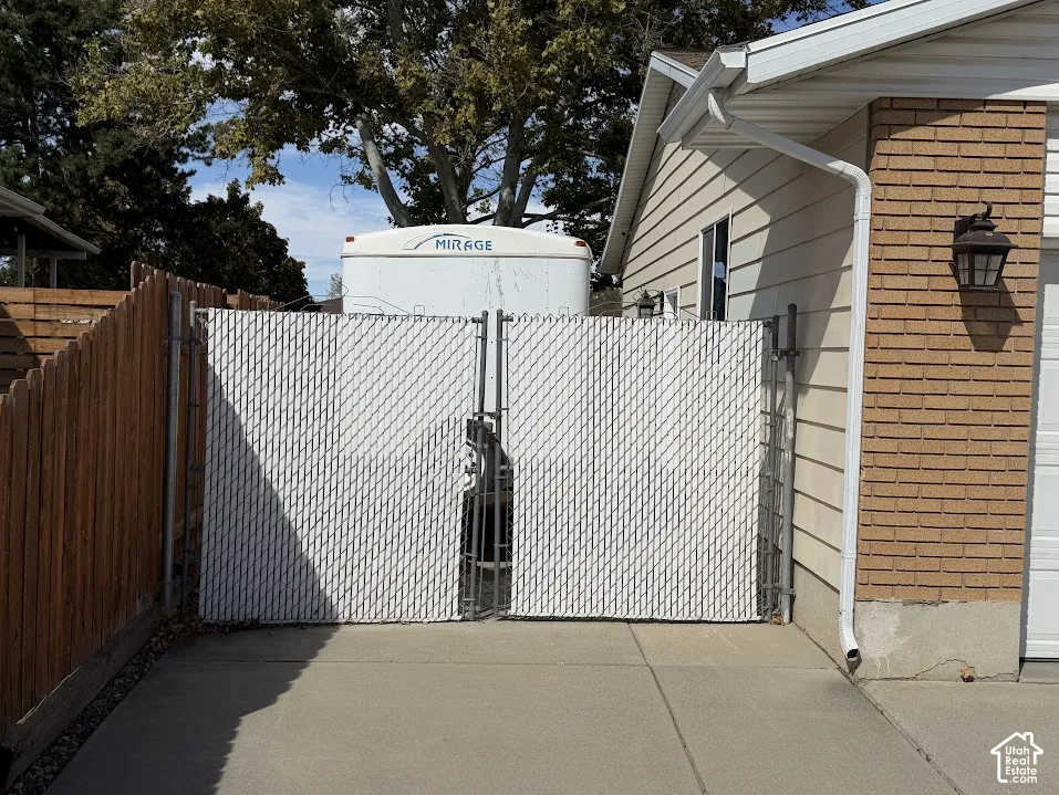 Chain link gate with privacy slats, wood fencing, concrete driveway, brick and siding exterior, exterior lighting fixture