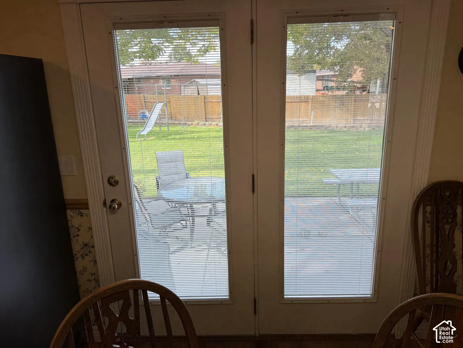 Double French doors with integrated blinds opening to a concrete patio and a fenced backyard with a manicured lawn