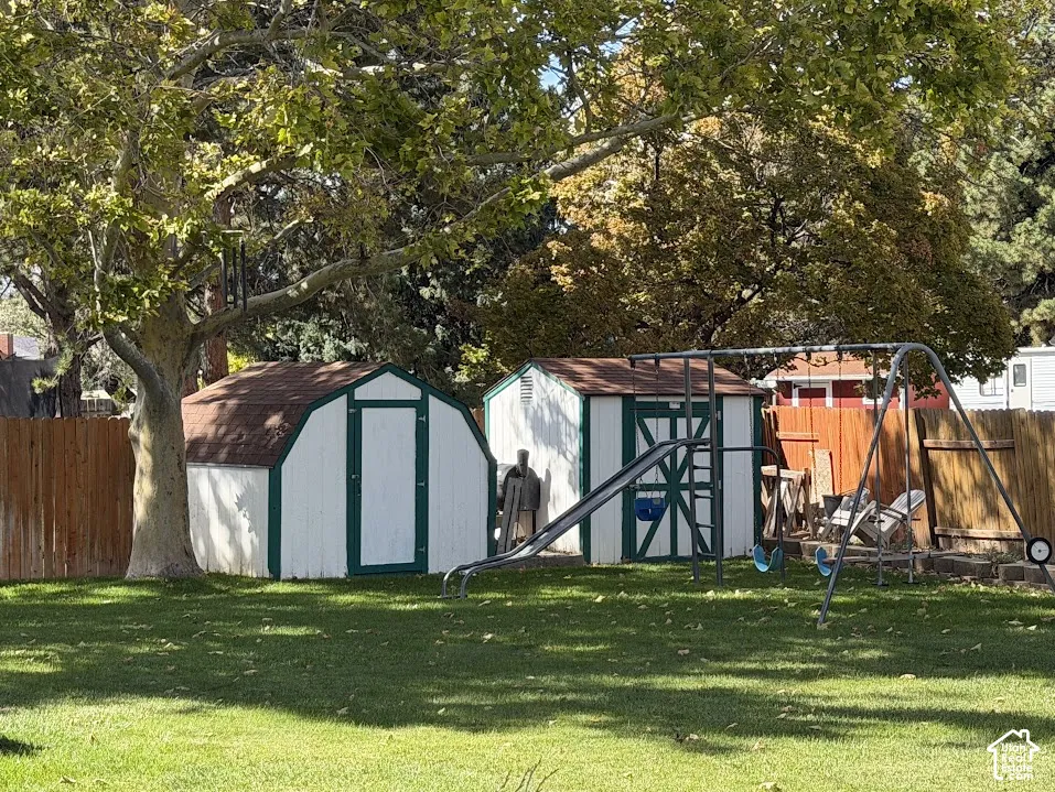 Expansive backyard featuring a mature tree, two storage sheds with gambrel roofs, and a wooden privacy fence