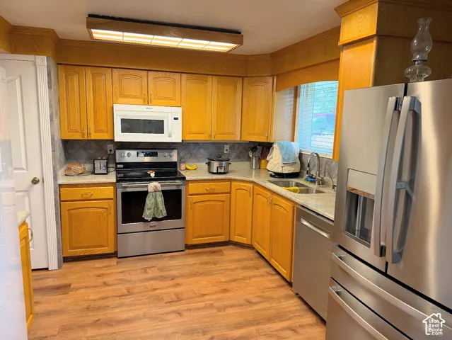 Kitchen featuring wood-finish cabinetry, stainless steel appliances, light-toned countertops, and a tile backsplash