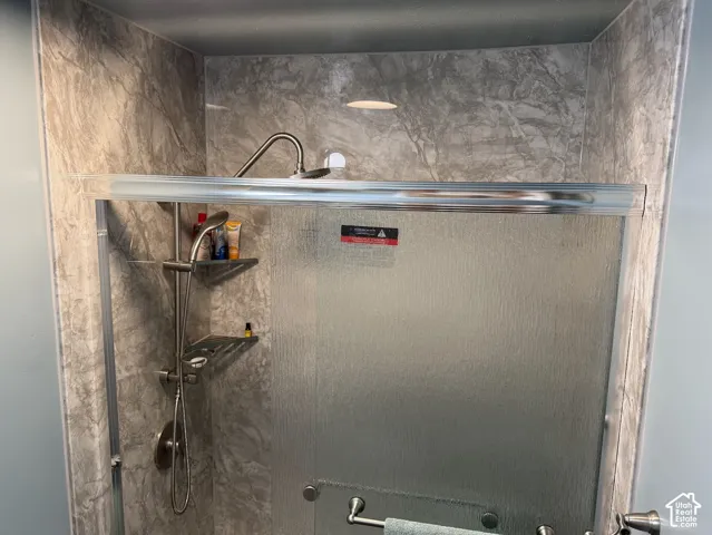 Enclosed shower with marble-finish walls, a brushed nickel shower system, and a glass-paneled door
