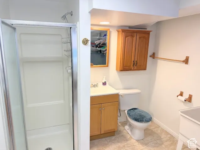 Tile flooring, vanity with wood-finish cabinetry, wall-mounted wood-finish cabinet, and a shower with a clear glass enclosure