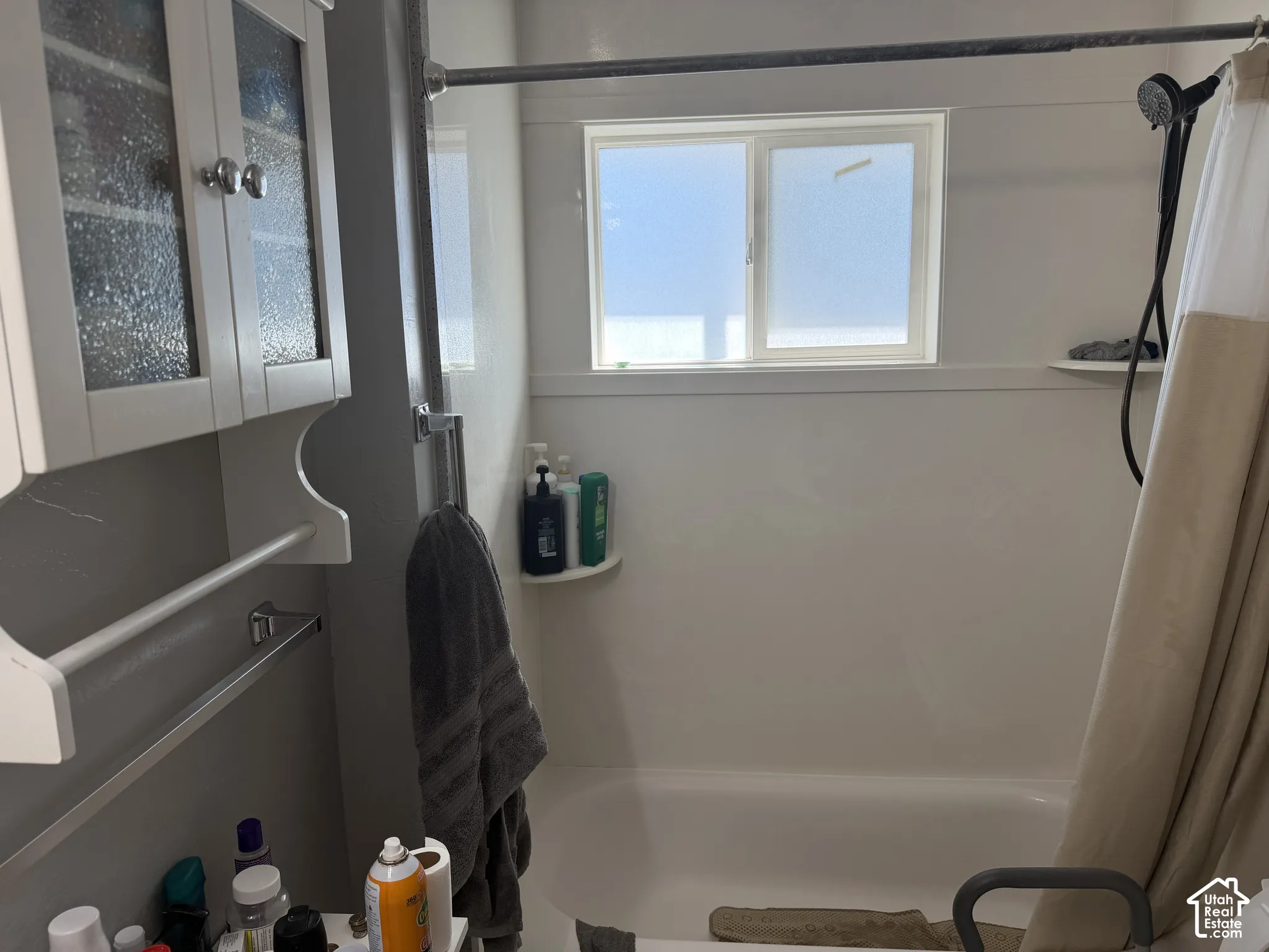 White bathtub with a wall-mounted shower head and a window with privacy glass