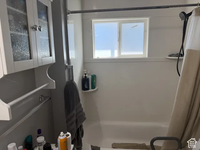 White bathtub with a wall-mounted shower head and a window with privacy glass