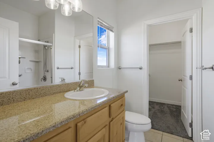 Vanity with integrated sink, stone countertop, wood-finish cabinetry, shower/tub combination, and tiled flooring