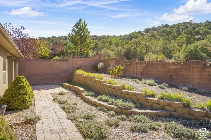 Expansive backyard retreat featuring tiered raised planter beds with drought-resistant landscaping, permeable paver pathways, mature tree backdrop, and brick boundary fencing