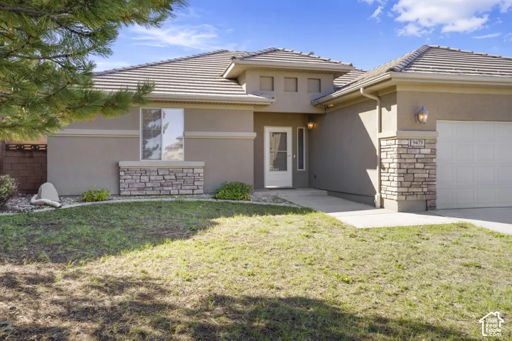 Stucco exterior with stone accenting, tiled roof, attached garage, and a concrete walkway leading to the entry