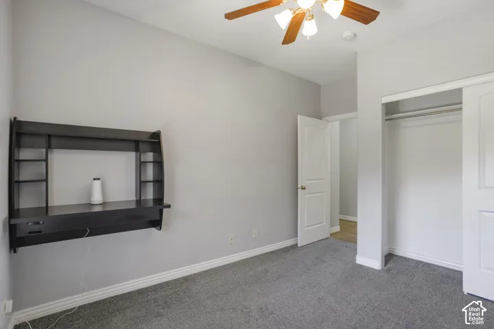 Carpeted room with a ceiling fan, built-in wall-mounted desk, and sliding closet doors