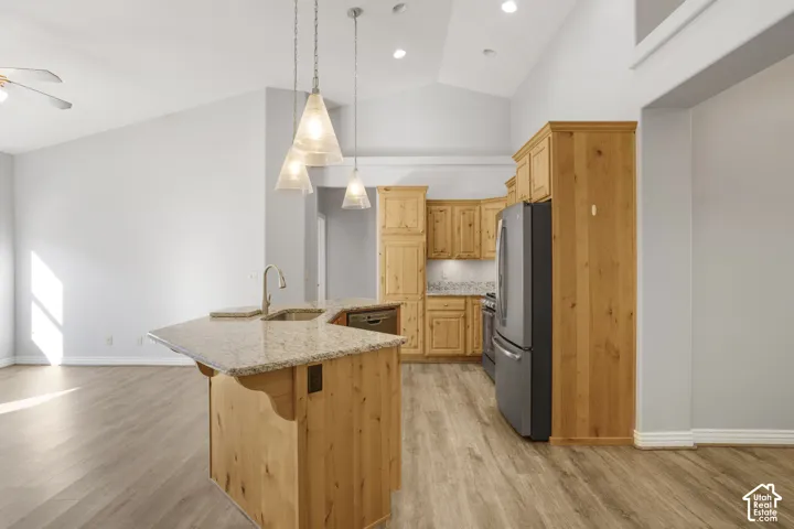 Kitchen featuring wood cabinetry, stainless steel appliances, a kitchen island with sink, and pendant lighting