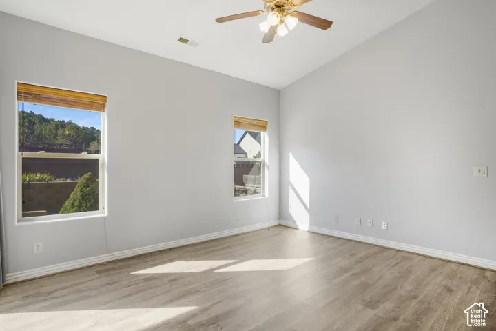 Vaulted ceiling with a ceiling fan, light wood-finish flooring, and two windows with wood blinds