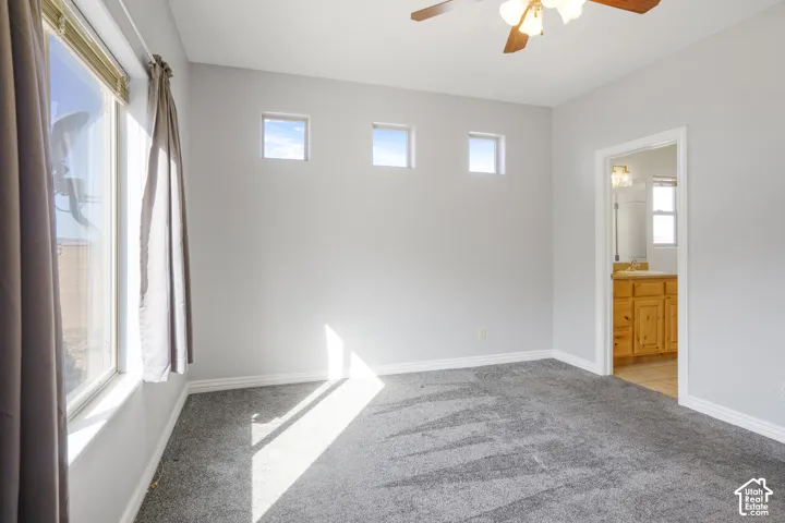 Wall-to-wall carpeting, multiple windows, ceiling fan with integrated lighting, and a neutral color palette
