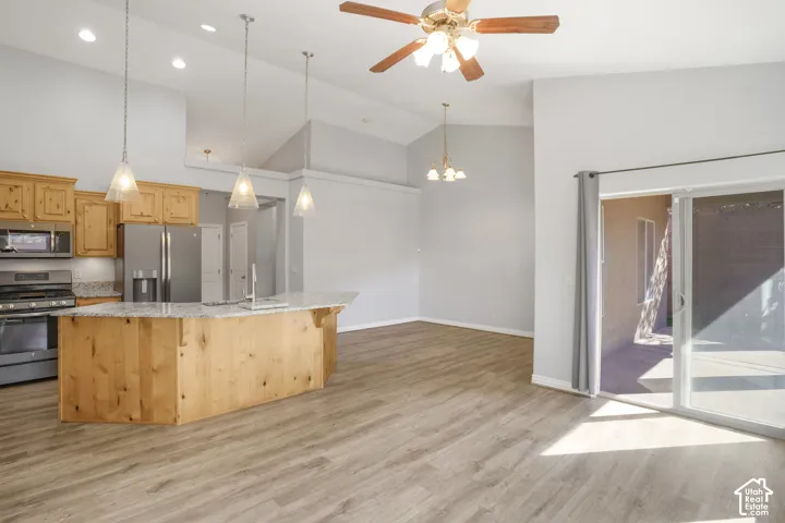 Vaulted ceilings, wood-finish flooring, stainless steel appliances, kitchen island with sink, and sliding glass door