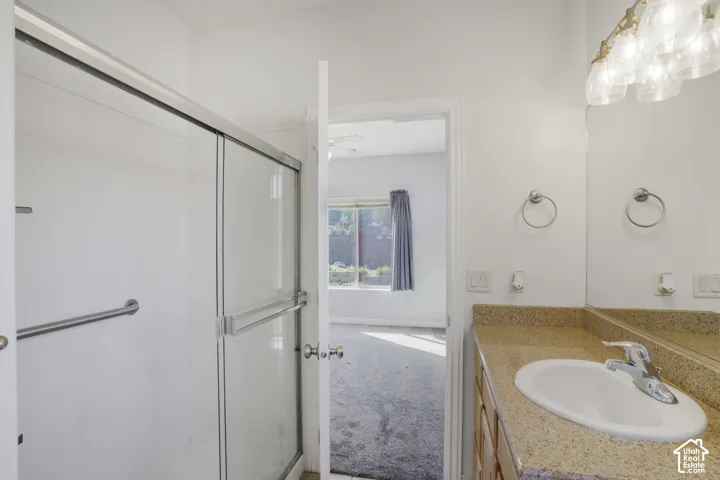Shower with sliding glass enclosure, single vanity with integrated sink, stone-finish countertop, and wall-mounted light fixture