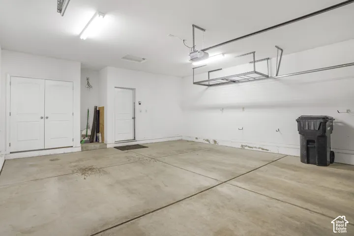 Attached overhead storage shelving, flush-mounted ceiling lighting, concrete flooring, and interior access doors