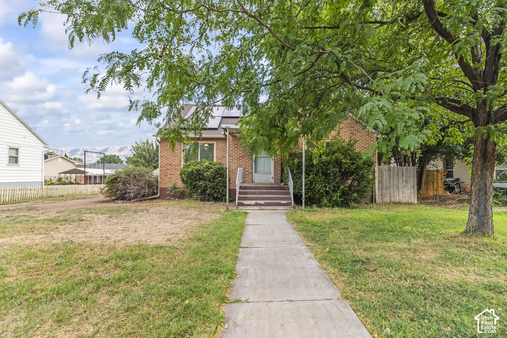 Brick exterior with a mature tree, concrete walkway, and established landscaping