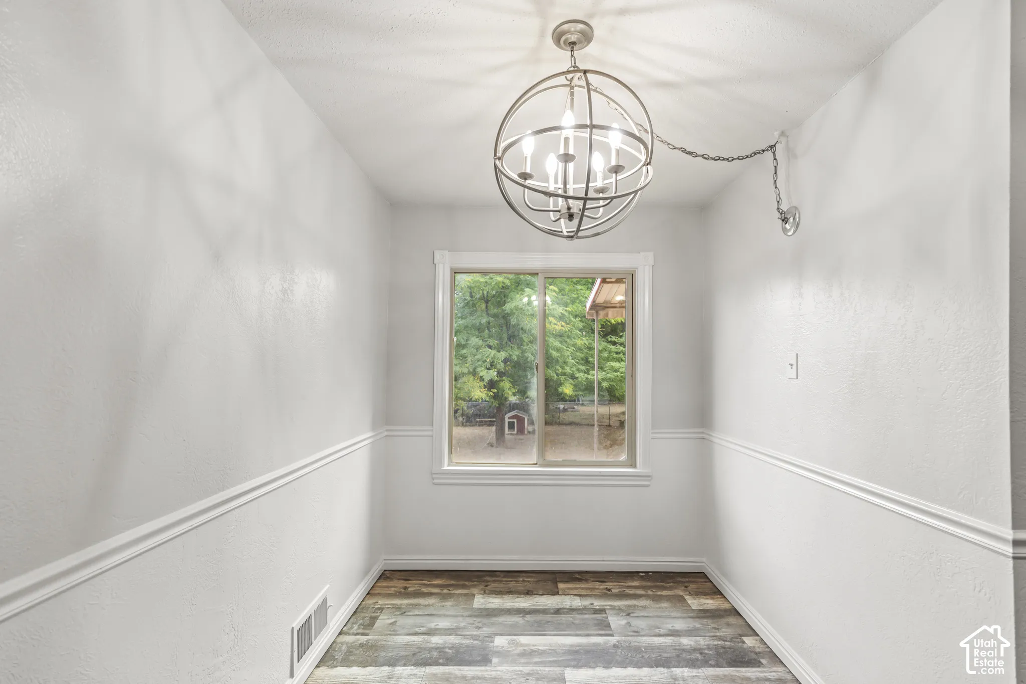 Wood-finish flooring, white walls, and a window with white trim, complemented by a contemporary orb chandelier