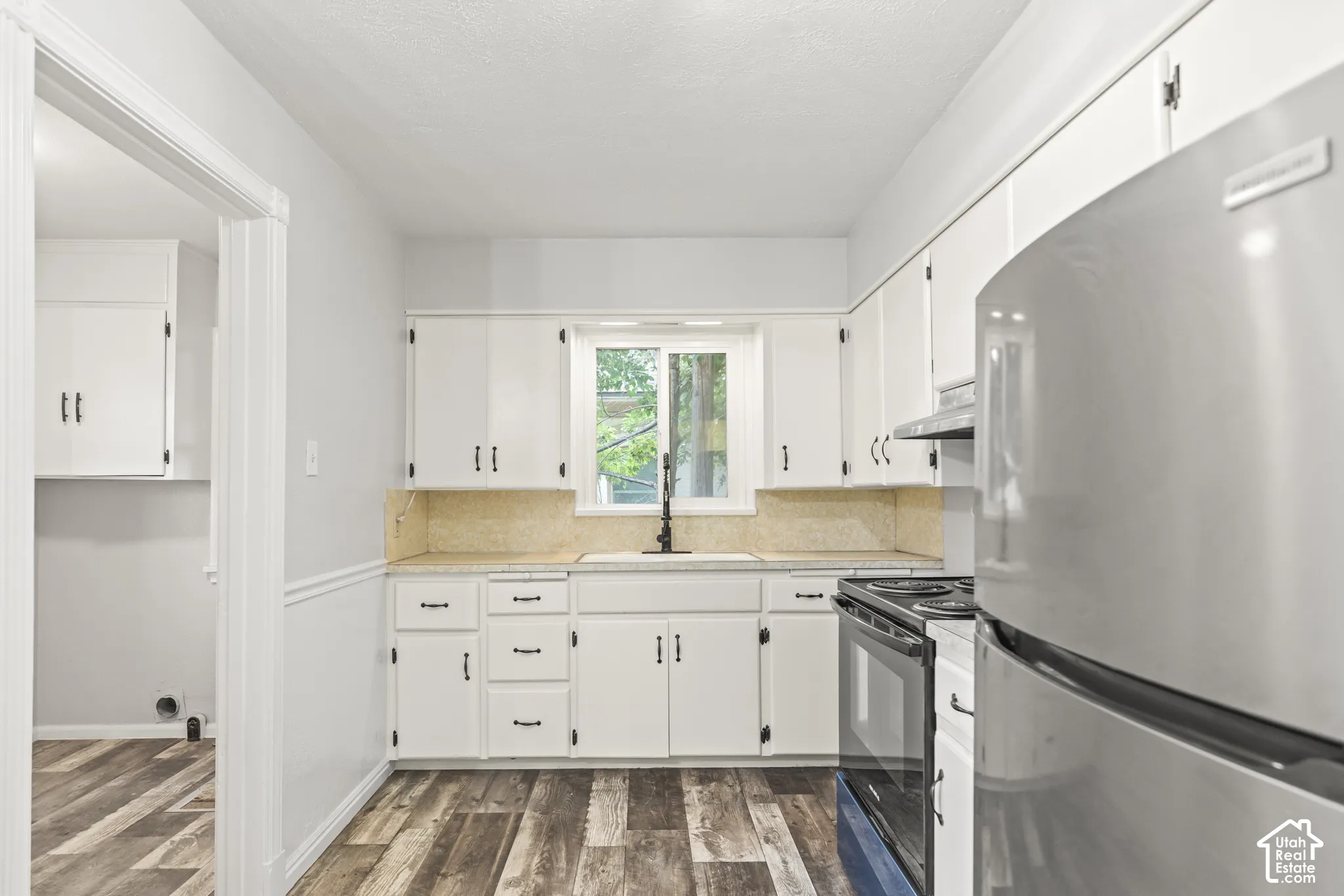 Bright kitchen featuring white cabinetry with hardware accents, stainless steel appliances including a gas range, light wood-finish countertops, and wood-finish flooring with a linear plank pattern