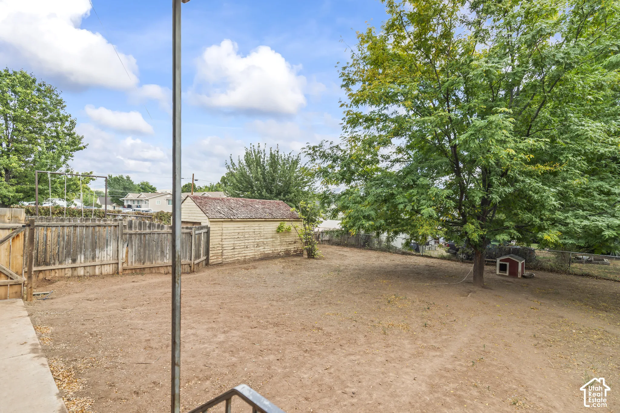 Spacious dirt arena with sturdy wood-finish fencing, mature shade trees throughout the grounds, and outbuilding structures