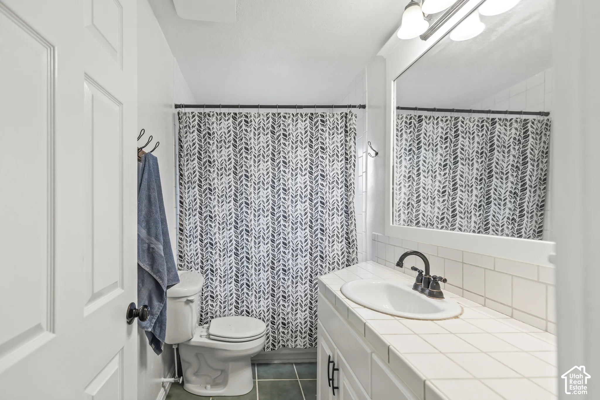 White subway tile backsplash, tiled countertop, built-in vanity cabinetry, and dark-finish fixtures
