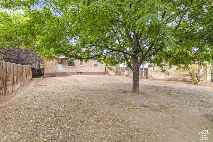 Expansive rear yard featuring mature trees, a wooden privacy fence, and a brick exterior dwelling