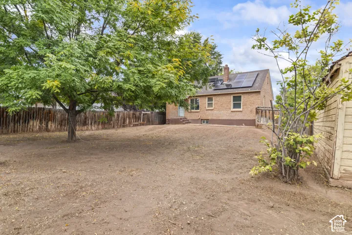 Expansive backyard with a mature tree, privacy fencing, and a brick exterior home featuring solar panels and an outdoor deck