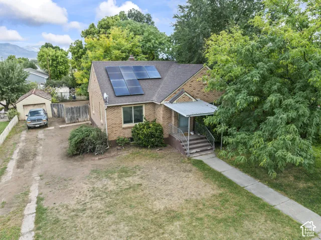 Brick exterior with solar panels, covered front porch, concrete walkway, and detached garage