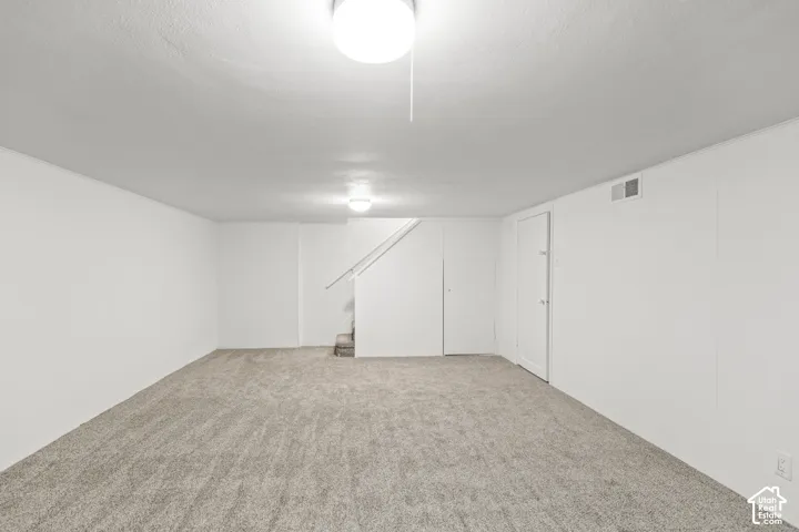Carpeted room with white walls, overhead ceiling lighting, and a closed door
