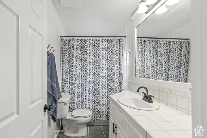White subway tile backsplash, tiled countertop, built-in vanity cabinetry, and dark-finish fixtures