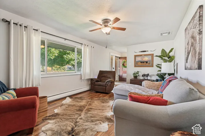 Bright, open living room featuring hardwood flooring, ceiling fan with integrated lighting, and large windows with natural light