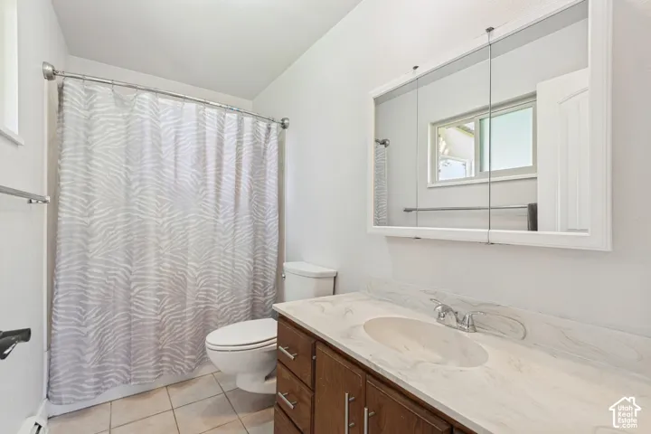 White walls, tiled flooring, wood-finish vanity with an integrated sink, tri-fold mirrored medicine cabinet, and a window