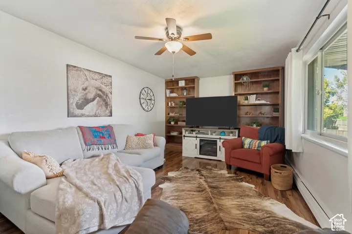 Wood-finish flooring, built-in shelving, white walls, ceiling fan with light fixture, and a window for natural light