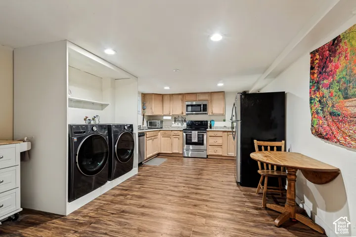 Integrated laundry area featuring built-in shelving, wood-finish flooring, recessed lighting, and a well-appointed kitchen with stainless steel appliances and light wood cabinetry