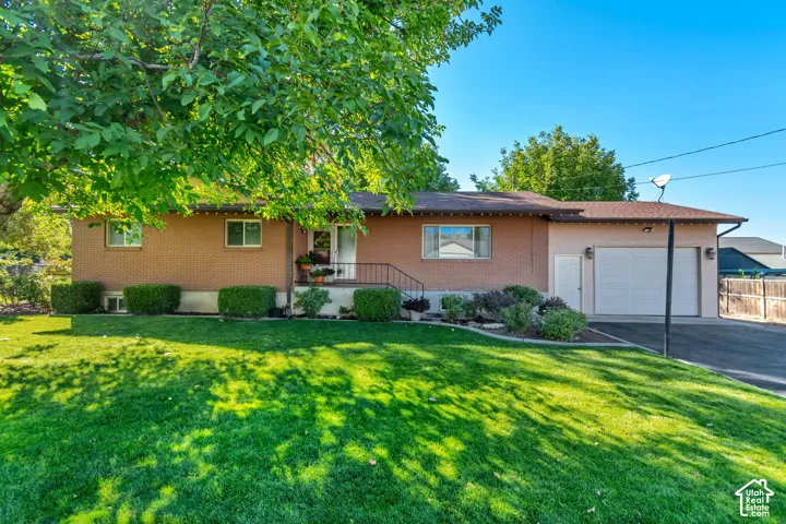 Brick exterior with an attached garage, paved driveway, and established landscaping