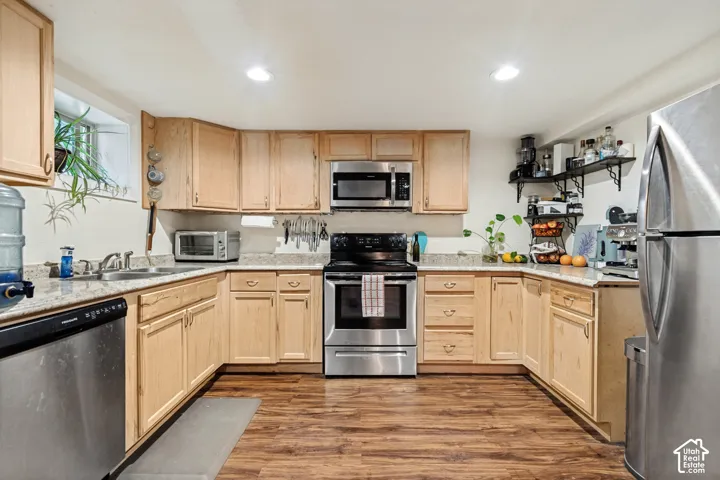 Wood-finish flooring, light wood cabinetry, stainless steel appliances, light-toned countertops, and recessed lighting