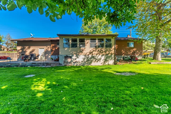 Expansive lawn with mature trees, a concrete patio, and a stucco exterior with multiple windows