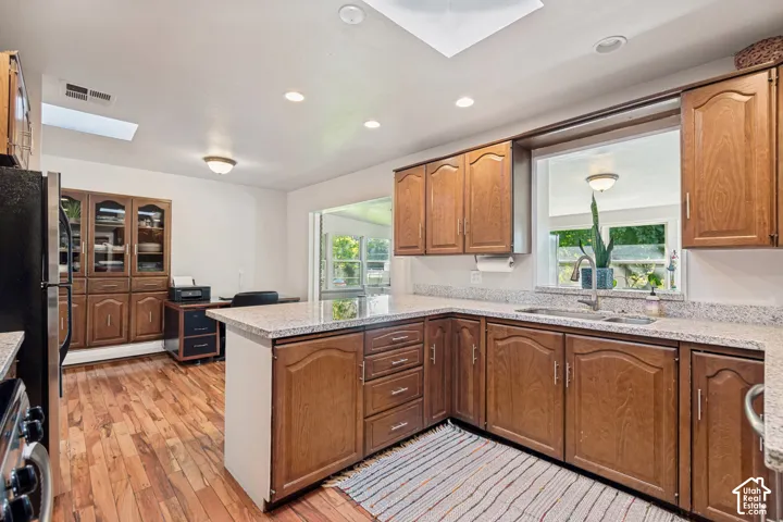Kitchen featuring wood-finish flooring, wood cabinetry, stone countertops, a stainless steel sink, and a skylight