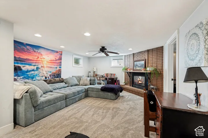 Recessed lighting illuminates the carpeted floor, featuring a brick fireplace with a mantel, a ceiling fan, and window openings