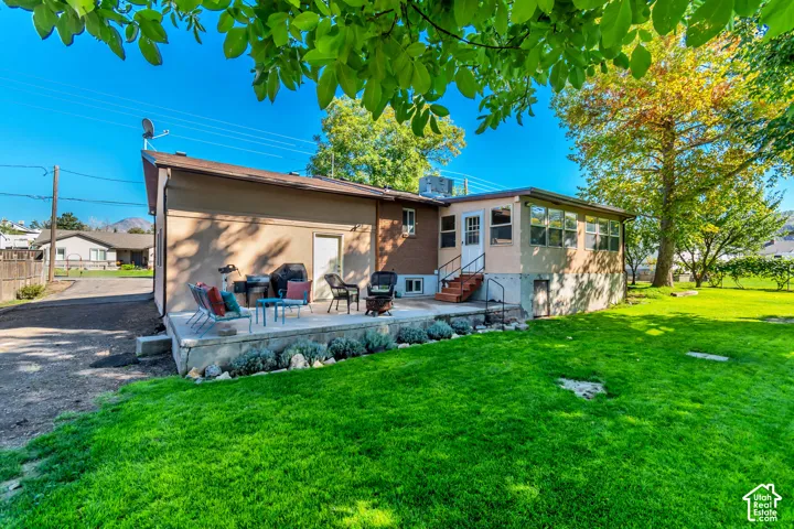 Expansive backyard featuring a manicured lawn, concrete patio, and a sunroom with multiple windows