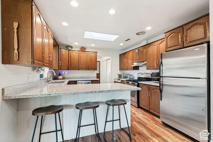 Hardwood flooring, stainless steel refrigerator, white beadboard kitchen island, recessed lighting, and a skylight