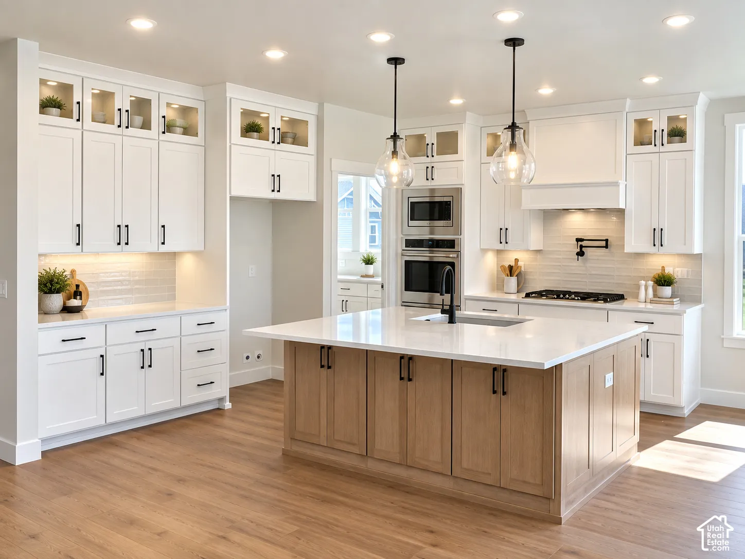 Spacious kitchen featuring an expansive island with a light wood finish, white shaker cabinetry, stainless steel appliances, wood-finish flooring, and pendant lighting
