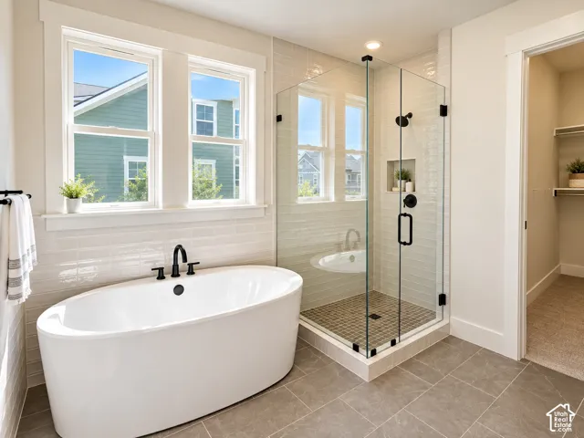Freestanding soaking tub with matte black fixtures, glass-enclosed shower with tile surround, and large format tile flooring