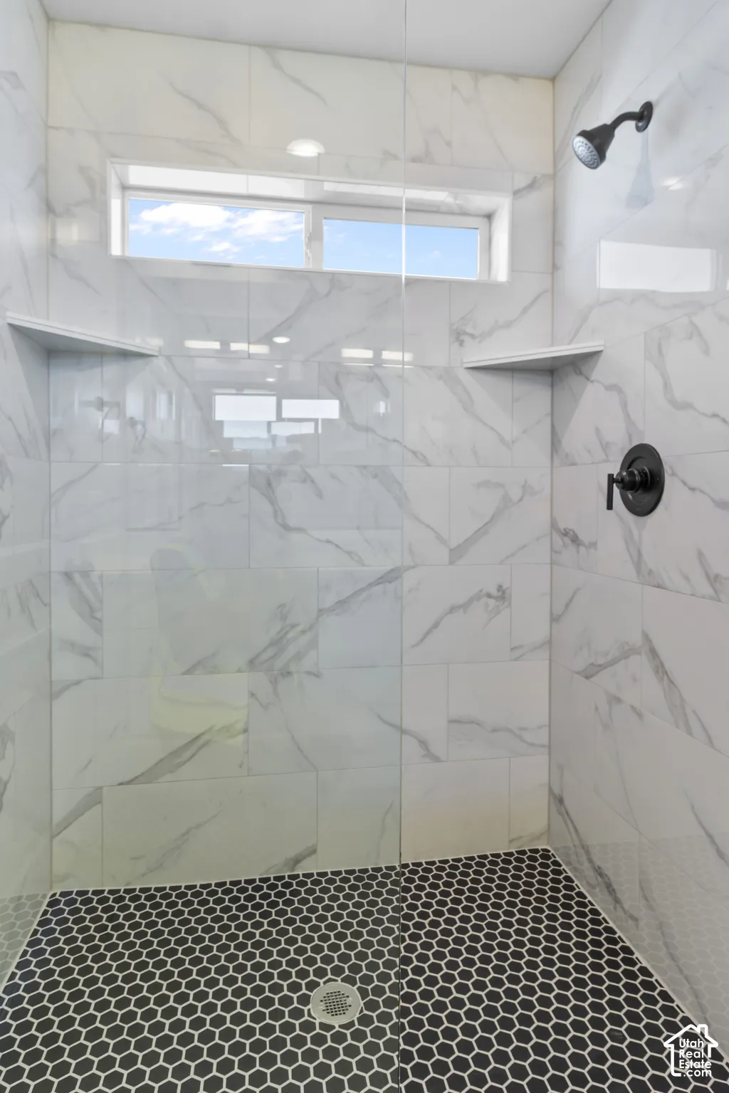 Walk-in shower with large format wall tiles, black hexagonal floor tiles, and a transom window