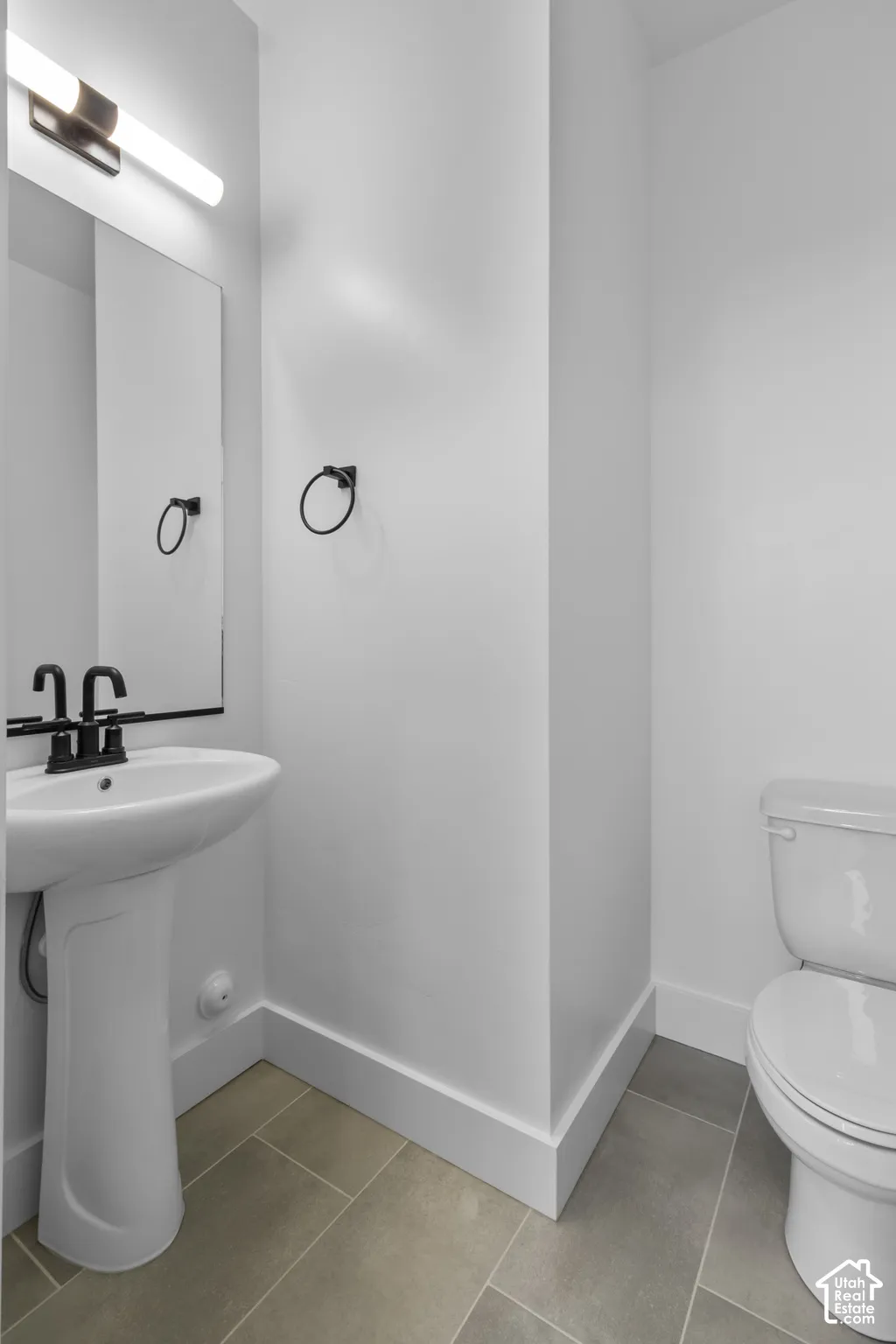 Pedestal sink with a black-finish faucet, rectangular mirror, and matte black lighting fixture