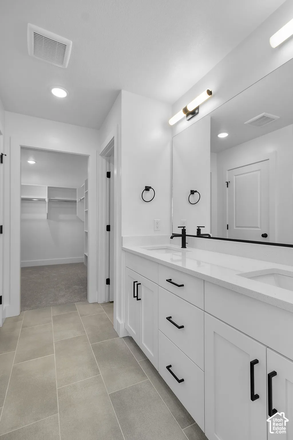 Dual vanity with white cabinetry and quartz countertops, matte black plumbing fixtures, large framed mirror, and tiled flooring