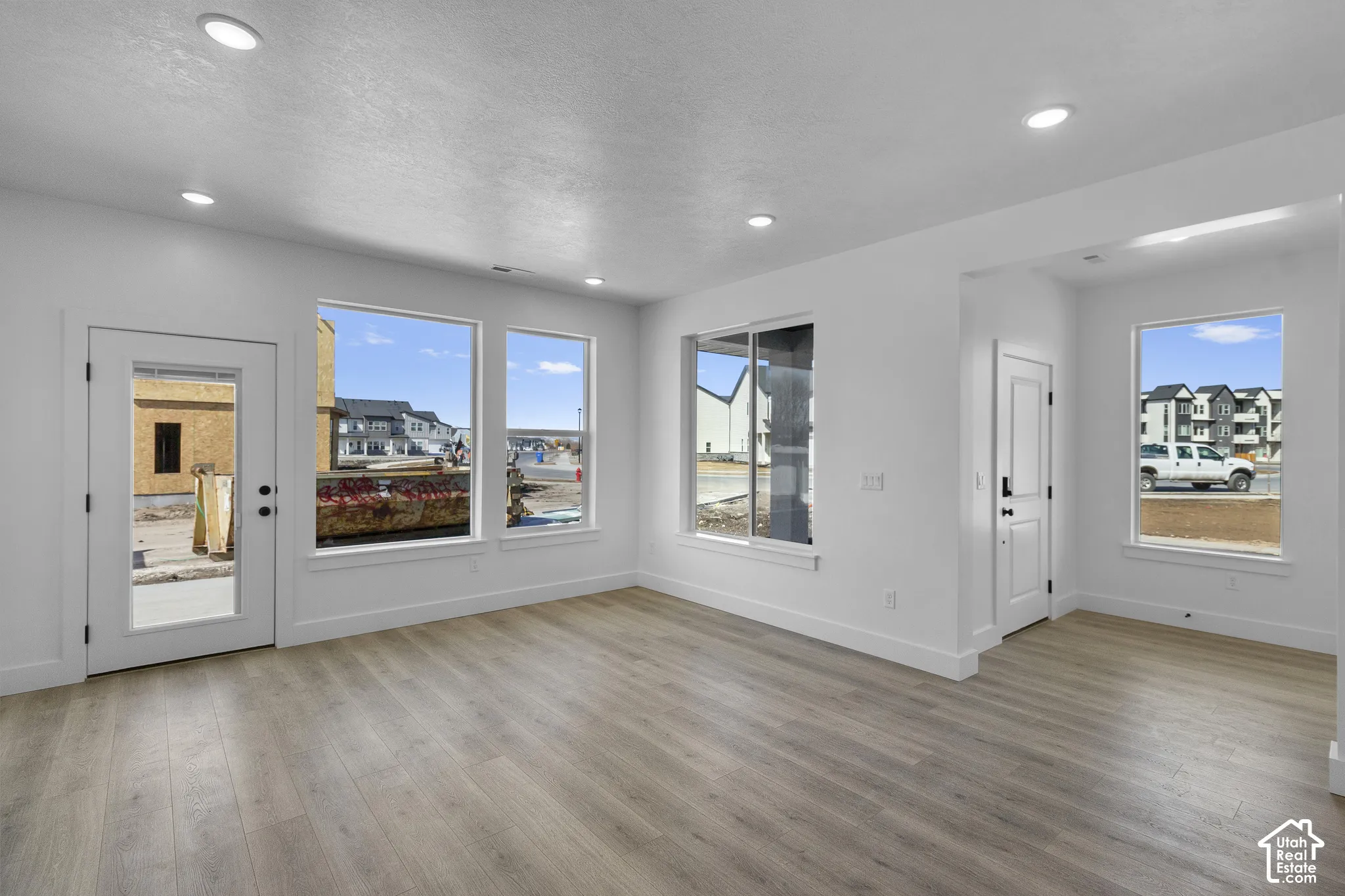 Recessed ceiling lighting, wood-finish flooring, white walls, multiple windows, and a glass-paneled door