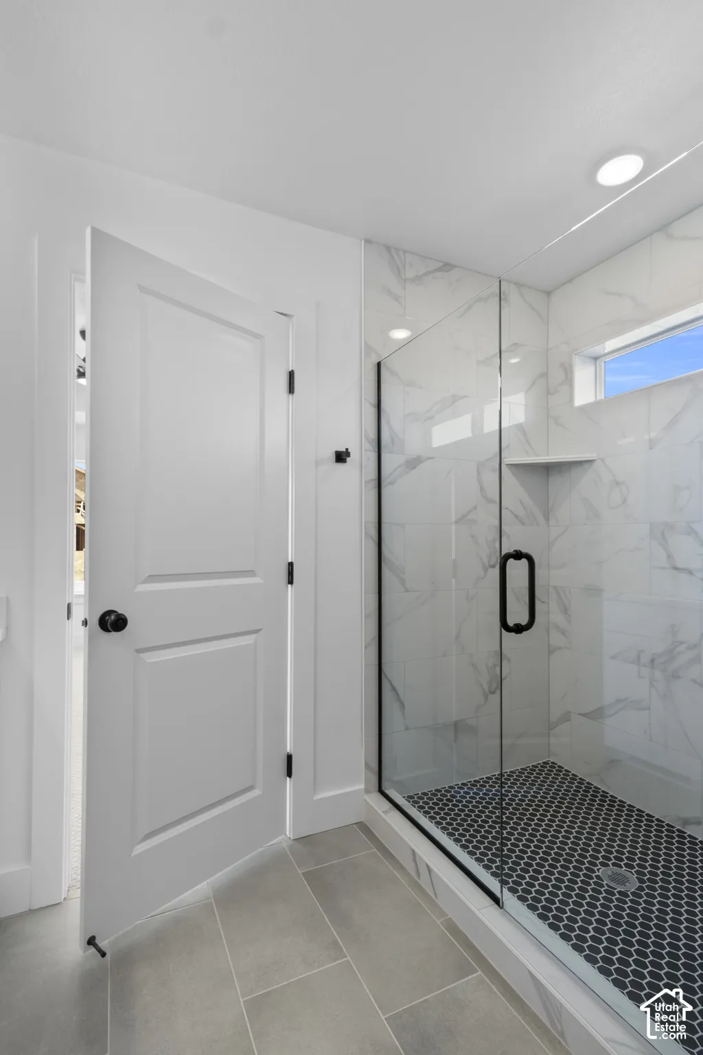 Walk-in shower with clear glass enclosure and black hexagon tile floor