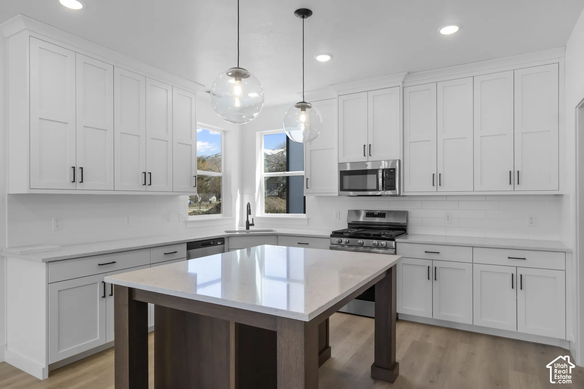 White shaker cabinetry, light countertops, stainless steel appliances, light wood-finish flooring, and recessed lighting